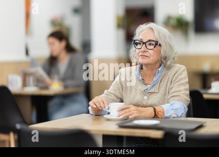 Seniorin sitzt allein am Tisch im Café und trinkt duftenden Kaffee Stockfoto