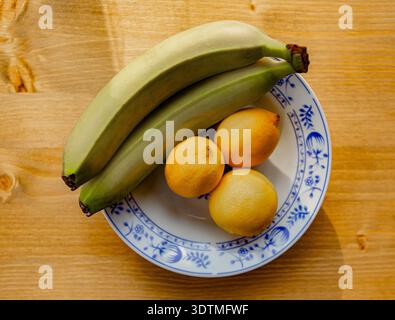 Ein horizontales Foto zeigt ein lebhaftes Arrangement aus frischen Bananen und hellen Zitronen auf einer Keramikplatte. Stockfoto