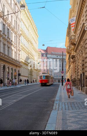 PRAG, TSCHECHISCHE REPUBLIK - 12. AUGUST 2024: Eine traditionelle rote Straßenbahnlinie 26 fährt entlang einer historischen Straße, die von klassischen Gebäuden in der Mitte gesäumt ist Stockfoto