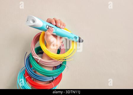 Die Hand hält einen modernen 3D-Druckstift mit leuchtendem, farbenfrohem Filament. Perfekt für Kreativität, MINT-Ausbildung und innovative Heimwerkerprojekte Stockfoto