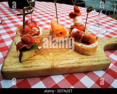 Verschiedene Canapés auf einem hölzernen Servierbrett über einer karierten Tischdecke. Dieses Bild stellt Gourmet-Snacks und stilvolle Essenspräsentation dar. Stockfoto