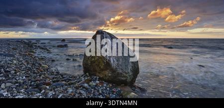 Felsiger Strand mit Felsbrocken an der Ostsee bei Sonnenaufgang unter dunklem Himmel mit dramatischen Wolken, Jasmund Nationalpark, Rügeninsel, Mecklenburg-Wester Stockfoto