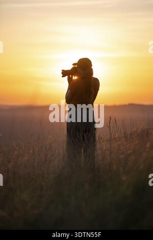 Junge Frau, die bei Sonnenuntergang Fotos macht, im hohen Gras steht, am Victoriasee, Uganda Stockfoto