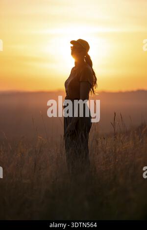 Junge Frau, die bei Sonnenuntergang im hohen Gras steht, Lake Victoria, Uganda Stockfoto