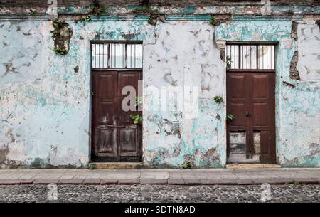 Vintage verlassene Kolonialgebäude mit Holztüren und Pflanzen aus den rissigen Wänden wachsen, Antigua, Guatemala Stockfoto