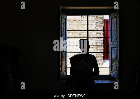 Silhouette einer Frau in einem dunklen Raum vor dem Fenster und der Sonne draußen Stockfoto