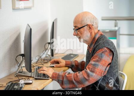 Senior-Mann, der am Schreibtisch arbeitet. Konzentrierter Senior-Mann, der am Computer am Schreibtisch arbeitet. Modell freigegeben Stockfoto