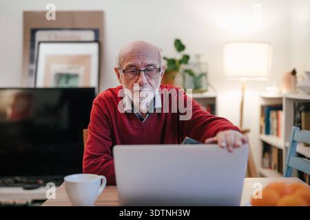 Senior Mann, der zu Hause Laptop benutzt. Senior-Mann, der abends zu Hause mit dem Laptop arbeitet. Modell freigegeben Stockfoto