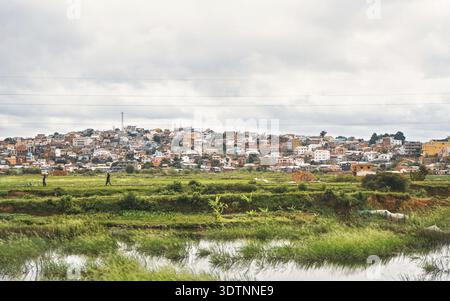 Antananarivo, Madagaskar - 24. April 2019: Typische Landschaft während des bewölkten Tages in der Nähe von Madagaskar Hauptstadt, Häuser auf kleinen Hügeln Hintergrund, mit Menschen Stockfoto
