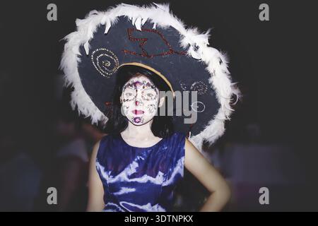Merida, Mexiko - 31. Oktober 2018: Frau als catrina gekleidet mit Blumenschädel Make-up und großem Hut mit Feder für den Tag der Toten 'Dia de los muertos' Stockfoto
