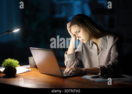 Besorgter freiberuflicher Mitarbeiter, der sich beschwert, online zu arbeiten und nachts einen Laptop zu überprüfen Stockfoto