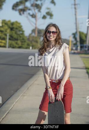 Schöne junge Frau mit Skateboard im Abendlicht Stockfoto