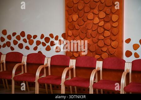 Reihe roter Polsterstühle vor einer dekorativen Holzwand in einem modernen Wartezimmer. Sauberes, organisiertes Innenleben, ideal für das Gesundheitswesen, das Büro Stockfoto