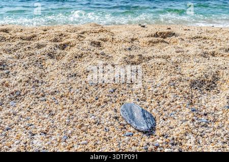 Horizontale Perspektive eines glatten grauen Steins am Cleopatra Beach, Alanya, Türkei, mit weichen türkisfarbenen Wellen. Küstenlandschaft mit Kopierraum Stockfoto