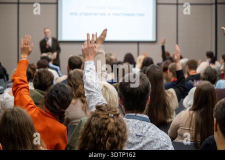 Das Konferenzpublikum hebt die Hände, um Fragen während der Präsentation zu stellen, motiviert die Teilnehmer im Konferenzraum, interaktive Seminaratmosphäre. Stockfoto
