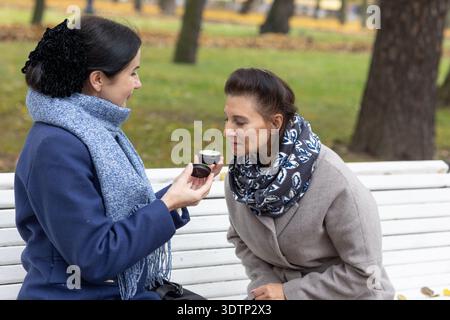 Kommunikation. Zwei weibliche Freunde treffen sich im Stadtpark im Freien und teilen während der kühlen Jahreszeit tagsüber emotionale Gespräche und Gesten. Stockfoto