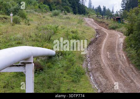 Kozjowa, Ukraine – 14. August 2013: Weiße Industrieleitung entlang einer steilen Feldstraße durch ein grasbewachsenes Feld mit dichtem Wald in Th Stockfoto