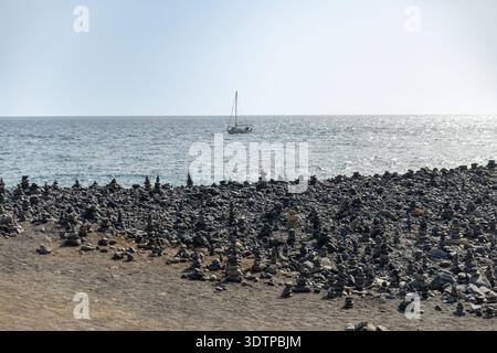 Rocky Beach mit Stone Cairns und Segelboot am Horizont unter dem ruhigen blauen Meereshimmel Stockfoto