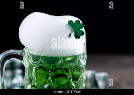 Gießender grüner Bierkrug mit Schaum für St. Patrick’s Day auf schwarzem Holztisch und schwarzem Hintergrund Stockfoto