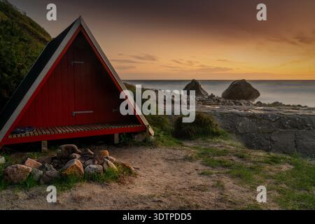 Ein kleines rotes Holzhaus mit A-Rahmen und Kamin an der Nordküste der Insel Bornholm bei Sonnenuntergang Stockfoto