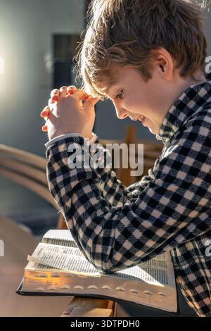Kindergebet über eine offene Bibel bei Tageslicht. Betender Junge. Stockfoto