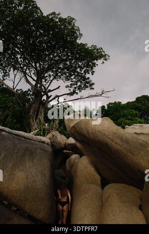 Langhaarige Frau in schwarzem Badeanzug, die zwischen Granit b krabbelt Stockfoto