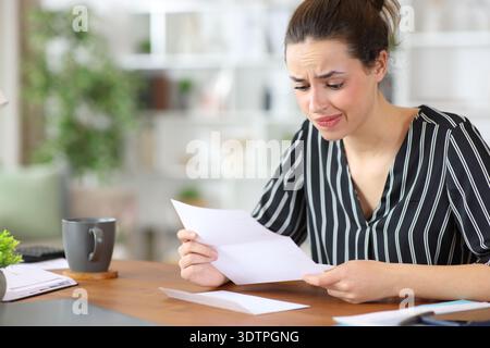 Enttäuschte Selbstständige, die Papierdokumente lesen und zu Hause arbeiten Stockfoto