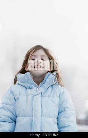 Lächelndes Mädchen in blauer Pufferjacke im Winter Stockfoto