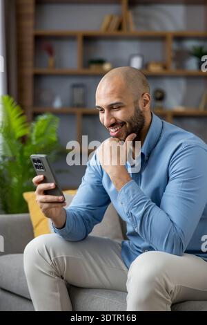 Ein lächelnder Mann findet Unterhaltung und Verbindung, während er auf sein Smartphone blickt, Freizeit und digitale Kommunikation bequem von zu Hause aus genießt Stockfoto