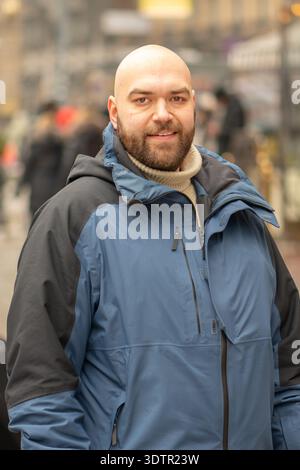 35-jähriger Mann in Winterjacke, der auf einer Stadtstraße unter Fußgängern steht Stockfoto