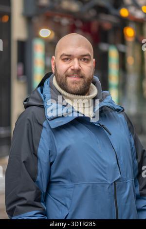 35-jähriger Mann in warmer Jacke, der im Winter eine Stadtstraße entlang läuft Stockfoto