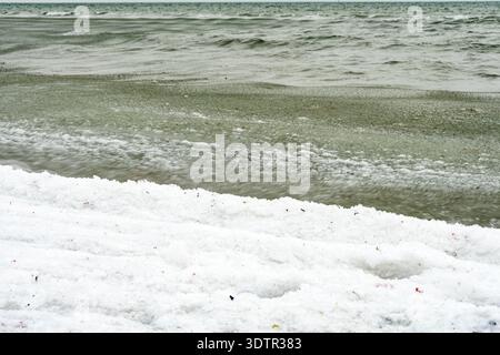 Schneebedeckte Küste mit sanften Wellen entlang einer kalten Küstenszene, die die Winterbedingungen und eisige Texturen am Wasserrand zeigt. Stockfoto