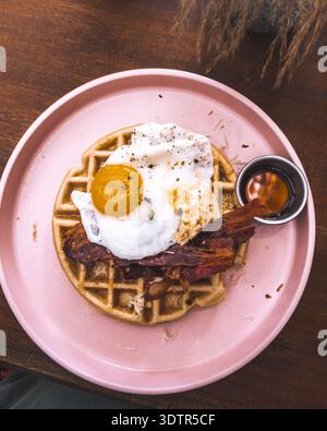 Herzhafte Waffeln mit Spiegelei und knusprigem Speck serviert auf rosa Teller im Holbox Café. Stockfoto