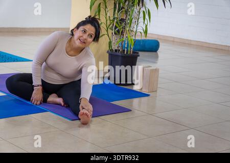 Frau, die eine sitzende Vorwärtsbeugung auf einer Yogamatte in einem Studio vorführt Stockfoto