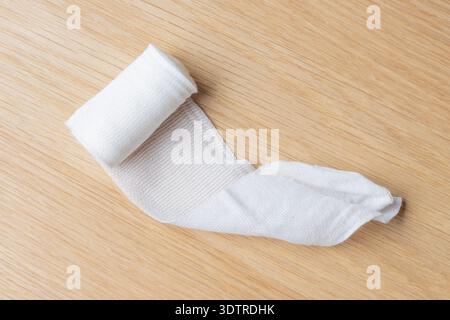 Ein sauber gerollter Verband liegt auf einer Holzoberfläche, bereit für die erste Hilfe oder Notfallversorgung. Stockfoto
