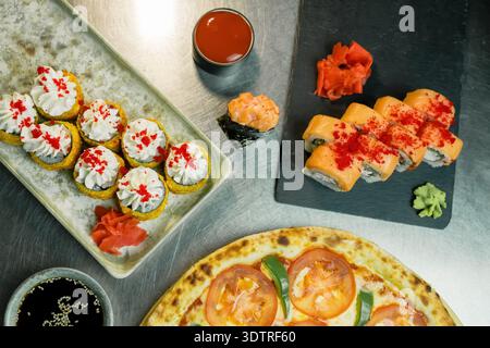 Eine bunte Präsentation von Sushi, Dessert Sushi Rolls und Pizza kunstvoll auf einer Metalloberfläche für ein köstliches kulinarisches Erlebnis Stockfoto