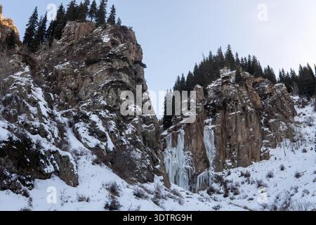 Atemberaubende Winterlandschaft mit Eisklippen und Kiefernwald in einer ruhigen Bergkulisse in der Abenddämmerung Stockfoto