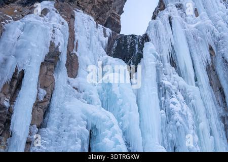 Eine majestätische Eiskaskade, die die felsigen Klippen hinunterfließt, in einer Winterlandschaft mit atemberaubenden blauen und weißen Eiszapfen, die anmutig hängen Stockfoto
