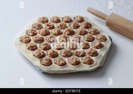 Rohe hausgemachte Teigtaschen, die in einer Metallknödelform zubereitet werden und mit Hackfleisch gefüllt sind. Traditionelles Konzept der osteuropäischen Küche Stockfoto