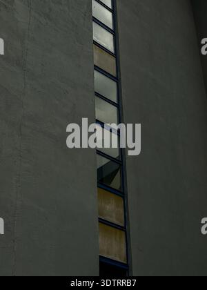Abstrakte architektonische Details mit vertikalen Fenstern und strukturierten grauen Wandflächen, beleuchtet durch sanfte natürliche Beleuchtung Stockfoto