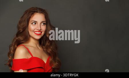 Fröhliche brünette Frau mit trendigem Make-up und braunem lockigem Haar wellige Frisur und rotem Lippen Make-up auf schwarzem Hintergrund Stockfoto