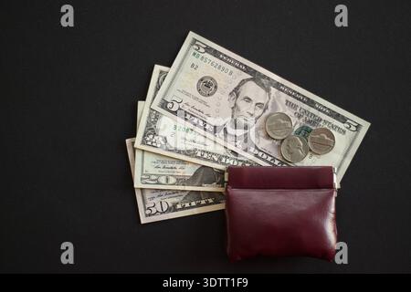 US-Dollar-Banknoten und -Münzen neben brauner Ledergeldbörse auf schwarzem Hintergrund Stockfoto
