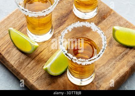 Tequila-Schüsse mit gesalzenen Rändern und Limettenscheiben, auf einem Holzbrett, eine Nahaufnahme Stockfoto