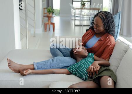 Mutter und Sohn sitzen auf hellem Sofa in hellem Haus, Mutter streichelt die Stirn und hält die Hand Stockfoto