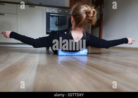 Frau, die sich auf Schaumstoffrolle auf dem Boden der Küche entspannt. Selbstpflege, Rückenentlastung und Stretching-Workout-Konzept. Stockfoto