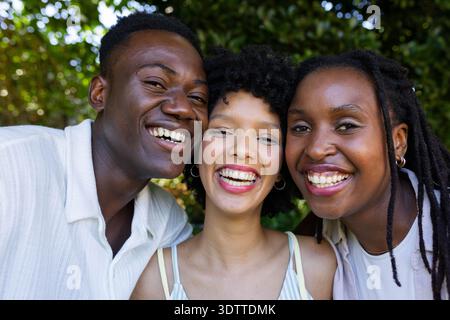 Afroamerikanische Freunde lachen in der Nähe des Parks, Button-up-Hemd, gestreiftes Tanktop, Creolen-Ohrringe Stockfoto