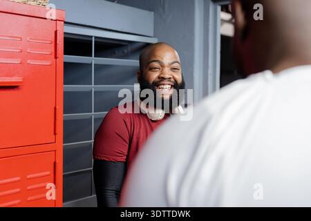 Afroamerikanische Männer lachen und plaudern im Korridor in der Nähe des roten Schließfachs mit Kopfhörern Stockfoto