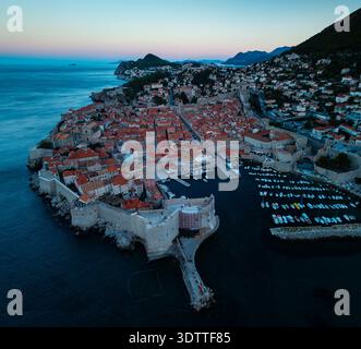 Aus der Vogelperspektive auf die alten Stadtmauern umschließen die Terrakotta-Dächer, während der Hafen unter dem schwindenden Licht leuchtet, Dubrovnik, Dubrovnik-Neretva Coun Stockfoto