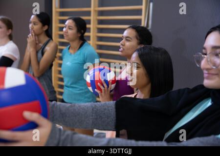 Abwechslungsreiches Teenager-Frauenteam im Sportbekleidung-Trainingsvolleyball in der Schulgymnastik rot-weiß-blaue Bälle Stockfoto