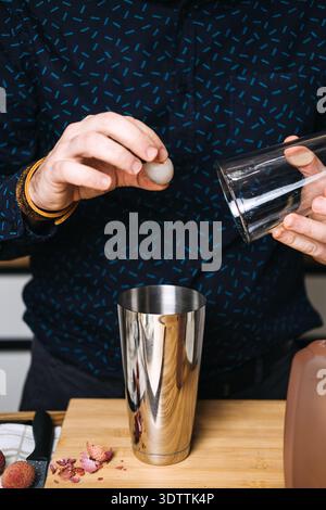 Der Barkeeper wirft geschälte Litschi in einen Cocktail-Shaker aus Edelstahl neben Obsthäuten und Glas. Craft-Cocktail-Bewegung, professioneller Barkeeper Stockfoto